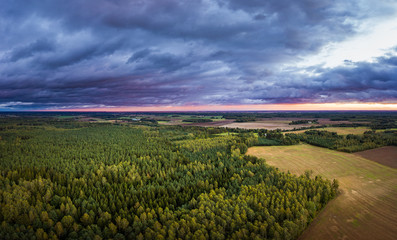 Aerial view on impressive storm clouds over forest in colorful sunset colors. Dark storm clouds covering the rural landscape. Intense rain shower in distance. 