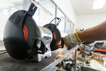 Man using Electric wheel grinding on steel with sparks in workshop, Bench grinding machine. 