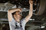 Fototapeta Przeznaczenie - Tired auto mechanic working on a chassis of a car in auto repair shop