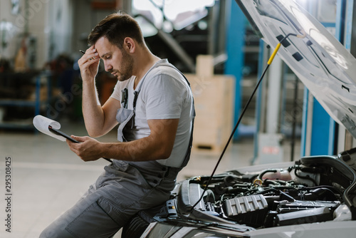 Young auto mechanic seeing potential problems while working on reports in a workshop