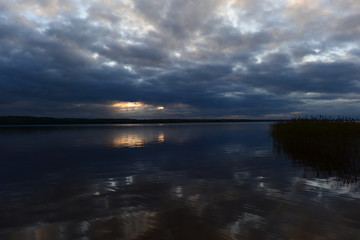 Wall Mural - Sunlight from dark clouds at sunset reflects on the lake water