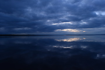 Wall Mural - Cloudy blue sky in sunlight from dark clouds reflected on lake water
