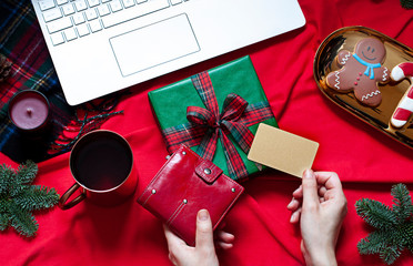 Buying Christmas presents with a credit card online concept flat lay. New Year top view on the red blanket with a keyboard and festive decoration.