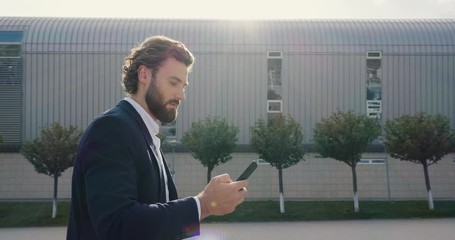 Attractive Man in Suit is walking down the streets of modern futures City. Man is using his Smartphone near Business district. Progressive Technology. Social Network. Busy Lifestyle. Phones. Apps.