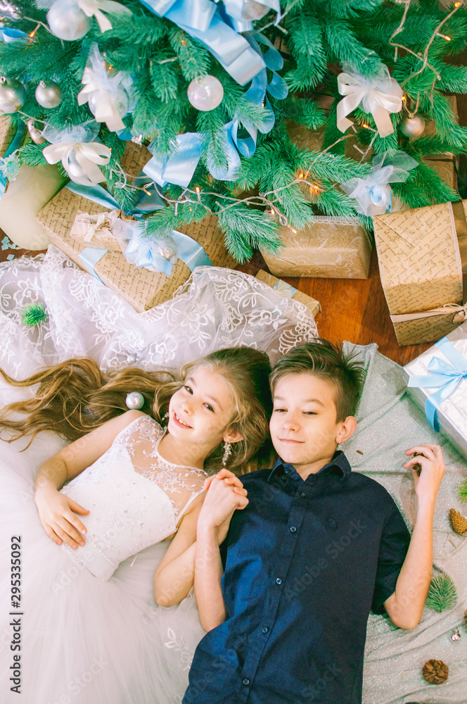 Children, brother and sister, are lying under the Christmas tree in holiday  dresses with gifts and silver confetti. Christmas mood Stock Photo | Adobe  Stock