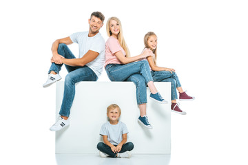 happy family sitting on cube and looking at camera on white