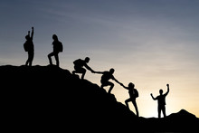 Silhouette Of People Helping Each Other Hike Up A Mountain At Sunset Background. Teamwork, Success And Goal Concept.