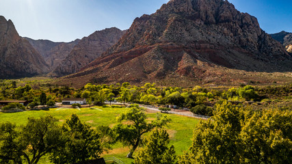 Beautiful view of famous Spring Mountain Ranch State Park near Las Vegas and Red Rock Canyon, Nevada during autumn with pink and red rock mountains, blue sky, green trees and grass, and purple hills