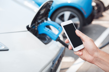 Wall Mural - Young adult man using smartphone and paying for charging electric car