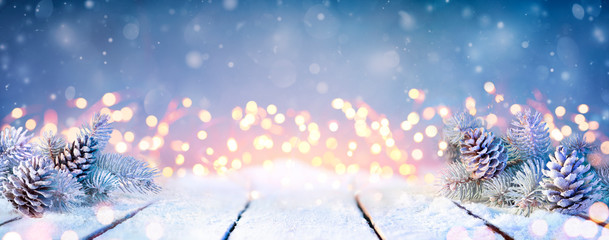 fir branches and pinecones on snowy table and christmas lights