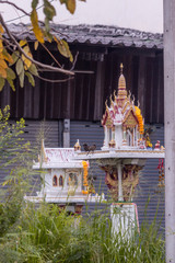 Chon Buri, Thailand - March 16, 2019: Closeup of white and gold private shrine set in green garden and backed by gray brown wall on Sukhumvit Road.