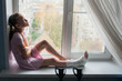 A teenage girl with a broken leg in a cast is sitting on a windowsill with crutches.