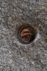 Open Eye Looking Through Round Hole In Stone Wall