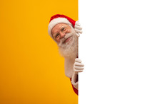 Happy Santa Claus Looking Out From Behind The Blank Sign Isolated On Yellow Background With Copy Space