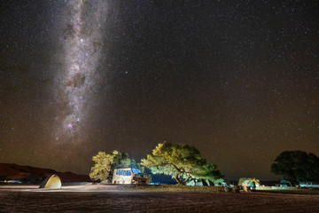 Wall Mural - night camping with illuminated tents under bright night sky full of stars and milky way.