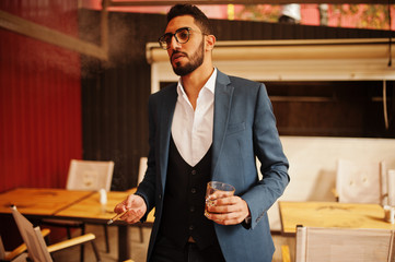 Wall Mural - Handsome well-dressed arabian man smoke cigar with glass of whiskey at balcony of pub.