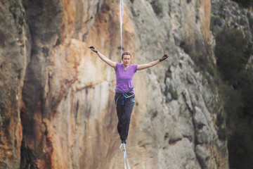 A woman is walking along a stretched sling. Highline in the mountains. Woman catches balance. Performance of a tightrope walker in nature.