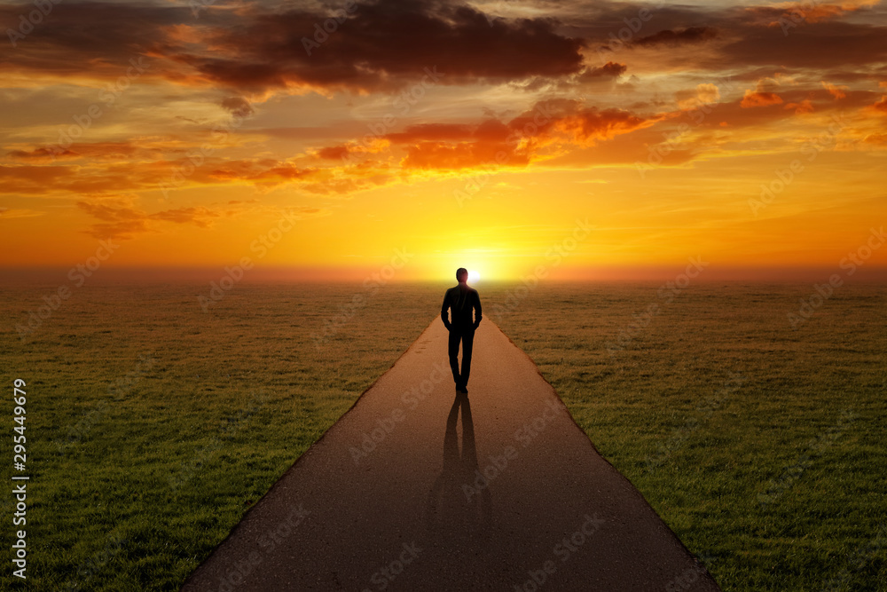 Man walking alone on a road towards the sunset - obrazy, fototapety, plakaty 