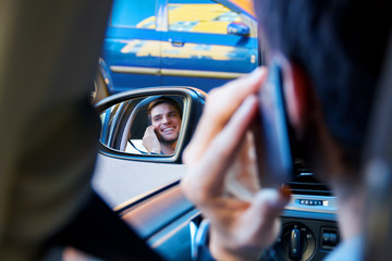 Wall Mural - Portrait of driver in car rear view window. Businessman is talking on smartphone behind steering wheel of auto. Young man is not attentively driving automobile. Guy is breaking rules of road.