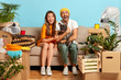 Photo of overjoyed married family couple rest on sofa during moving day, moved into new apartment, play with black pedigree bulldog, many packages with household items around. Two renters in abode