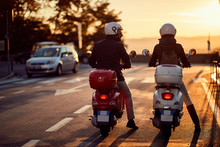 Couple Riding Motor Scooter On Road At Sunset.