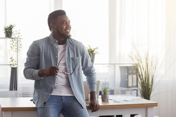 Happy startup owner leaning on office desk and looking aside