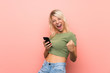 © luismolinero - Young blonde woman over isolated pink background with phone in victory position