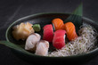 Close up side view of assorted sushi sashimi nigiri set on dark stone slate background. Salmon, tuna, mackerel fish on rice served with sprouts, wasabi and ginger on bamboo leaf. Traditional food