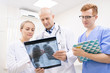 © pressmaster - Two doctors discussing x-ray of lungs while young intern making notes