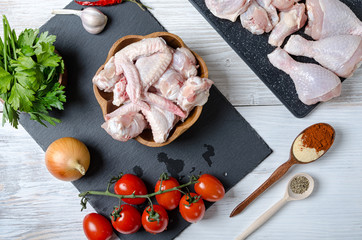 raw chicken wings and chicken thighs, ingredients for cooking, seasoning vegetables and chicken on a wooden table, top view