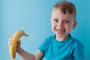 Wall Mural - Little Boy Holding and eating an Banana on blue background, food, diet and healthy eating concept