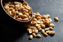 Round wooden bowl with roasted peeled peanuts closeup, salty beer snack on dark background