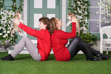 Happy mom and son pose on green grass with two cute little husky puppies