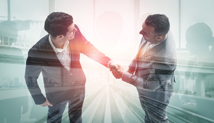 Wall Mural - Double exposure image of business people handshake on city office building in background showing partnership success of business deal. Concept of corporate teamwork, trust partner and work agreement.
