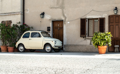 Wall Mural - Small vintage italian car. Beige color old car in front of old house facade and flowers..