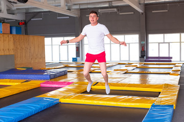 Fitness, fun, leisure and sport activity concept - Handsome happy man jumping on a trampoline indoors