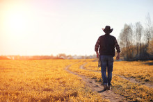 A Man Cowboy Hat And A Loso In The Field. American Farmer In A Field Wearing A Jeans Hat And With A Loso. A Man Is Walking Across The Field In A Hat