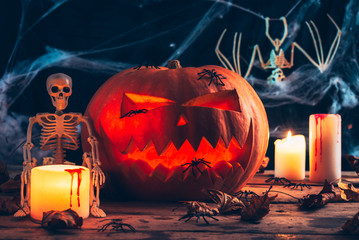 Halloween decor, Jack's Lantern band with glowing eyes, mystical glow, spider web,dry leaves, dark background, burning candles, skeleton bones