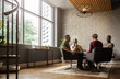 © JonoErasmus - Wide shot of casual seated diverse business meeting in modern open workspace with large windows and sunlight shining in