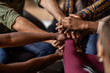 © JonoErasmus - Cropped close of diverse business people putting their hands on top of each other wearing casual clothes and african patterns.