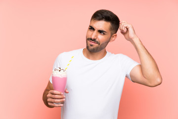 Wall Mural - Young man with strawberry milkshake over isolated pink background having doubts and with confuse face expression