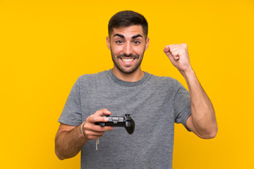 Young handsome man playing with a video game controller over isolated yellow background