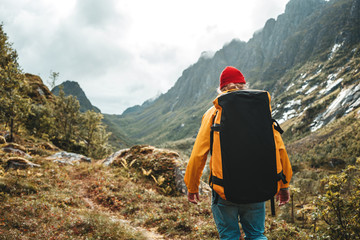 Wall Mural - Back view of man tourist with backpack standing in front of the mountain massif while journey by scandinavian. Male traveler wearing yellow jacket explore national park and hiking outdoor landscape