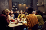 Fototapeta  - Group of young friends playing guessing game while sitting at table during dinner party in dark room, copy space