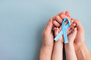 Man and child hands holding light blue Prostate cancer awareness ribbon on a light background. Medicine and healthcare concept, Men's health. Copy space, top view