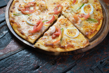 Closeup of fresh tasty pizza with seafood, tomato, paprika and mozzarella cheese isolated on rustic wooden background