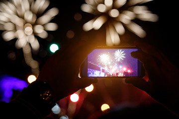 Silhouette of hands with mobile cell phone to take a photo of fireworks.