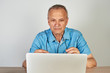 © amixstudio - Elderly Caucasian man in glasses with a serious expression on his face working on a laptop at his desk on a white background