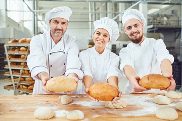 Bakers hold bread in their hands in bakery.