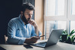 © foxyburrow - Professional sitting in office in front of laptop. Developer thinking on solutions for work. Home-based student getting distant education. Young serious bearded man in blue shirt working on desktop.